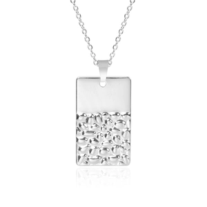 Vue macro d'un pendentif rectangulaire argenté aux textures lisses et martelées