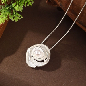 Detail of silver rose necklace with white pearl on snake chain over natural wood