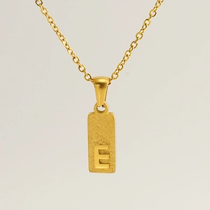 Macro shot of rectangular gold pendant with embossed letter E on a fine link chain