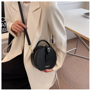 Detail of a round black leather crossbody bag with gold zippers worn by a model in a blazer