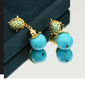 Macro detail of turquoise drop earrings with gold hollow frame on a black velvet box