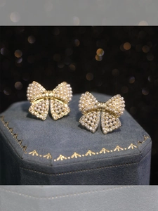 Close-up of golden bow earrings with pearls and zircons on blue velvet jewelry box