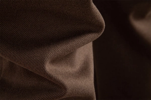 Macro shot of dark brown knitted fabric texture with soft folds on casual men's trousers