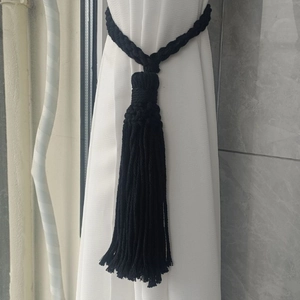Detail of handwoven black cotton curtain tieback with dense fringe on a white drape