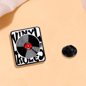 Close-up of retro Vinyl Rules enamel pin with black rubber clutch on orange background