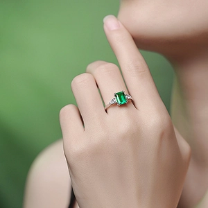Elegant silver ring with square emerald green gemstone and side diamonds on finger