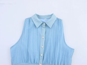 Detail shot of light blue sleeveless dress with pleated fabric texture and white buttons