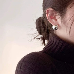 Close-up of a silver spherical stud earring worn by a model in a minimalist style
