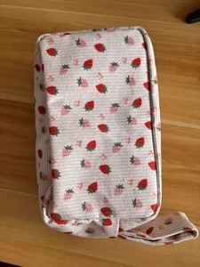 Detailed close-up of pink corduroy pouch with strawberry pattern and handle on wood