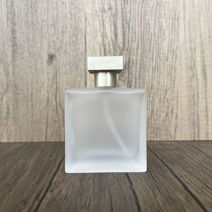 Close-up of frosted square glass perfume bottle with silver cap on wooden surface