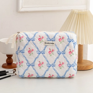 Close-up of quilted floral cosmetic bag with blue bows, pink roses and cream zipper