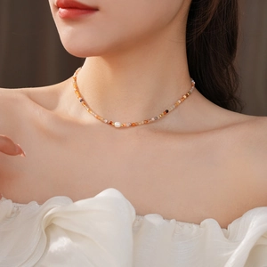 Close-up of beaded necklace with orange gemstones and a freshwater pearl on a model