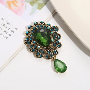 Vintage gold brooch with teardrop green gemstone and blue rhinestones on white surface