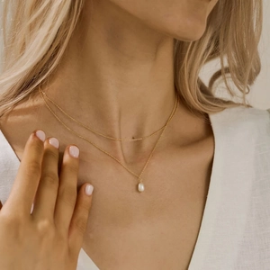 Double-layered gold stainless steel necklace with white pearl pendant on a model