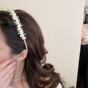 Detail of elegant white fabric rose headband with green silk ribbons on a gold base