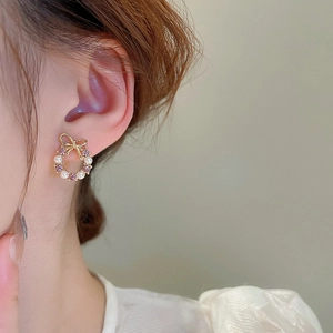 Close-up of bow wreath stud earring with pink zircon and white pearls on ear