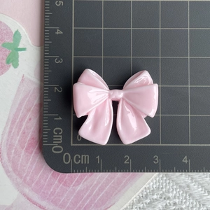 Close-up of pink resin bow accessory measuring 2.5cm width on a black grid scale mat