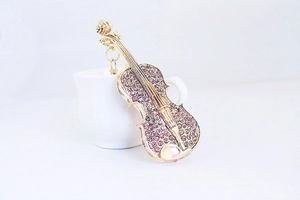 Détail d'une broche violon dorée avec strass scintillants posée sur une tasse blanche