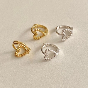 Flat lay of minimalist silver and gold heart earrings on a warm beige textured background