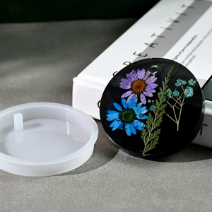 Macro shot of circular silicone mold and resin floral pendant with dried daisy inlay