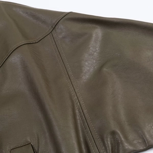 Detailaufnahme der olivgrünen Kunstleder-Textur und der präzisen Nähte an der Fliegerjacke
