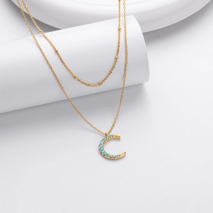 Detailed view of gold double layer necklace with turquoise moon pendant on white display