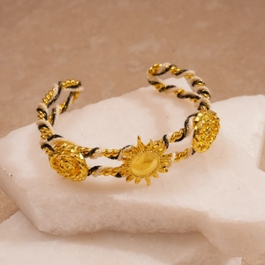 Detail of woven gold cuff bracelet with sun motifs on decorative white mineral stones