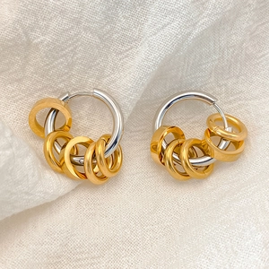 Detail of two-tone stainless steel hoop earrings with hanging golden rings on fabric