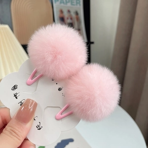 Close-up of fluffy pink faux rabbit fur ball hair clips on a white display card