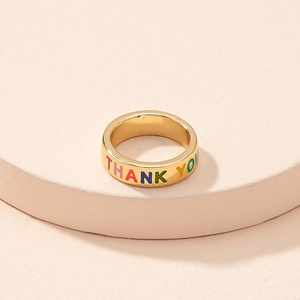 Macro shot of gold-plated ring featuring colorful THANK YOU engraving on a beige stand