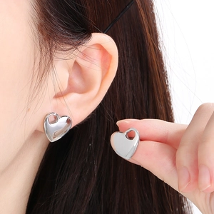 Close-up of heart-shaped silver stainless steel stud earrings worn on a model's ear