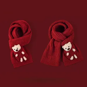 Detail of red knitted winter scarf with cute plush bear charms and coarse knit texture