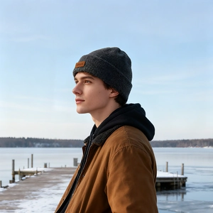 Deep grey knit beanie with leather logo patch worn in an outdoor winter setting