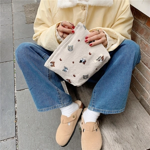 Detailed shot of a cream canvas pouch featuring cute cat embroidery and side brand label