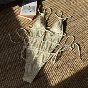 Costume intero a costine color crema con dettagli cut-out e lacci su tappeto di paglia