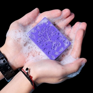 Detail of purple soap bar with intricate floral ethnic patterns held in foamy hands