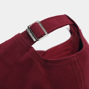 Detailed close-up of the adjustable silver metal buckle on a burgundy cotton baseball cap