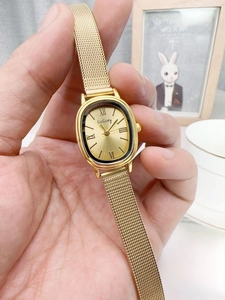 Detailed close-up of retro oval gold quartz watch with a milanese mesh band and roman numerals
