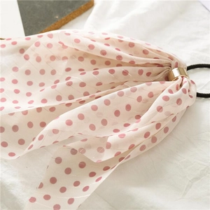 Detail of white semi-transparent polka dot bow hair tie with a gold metal buckle accent