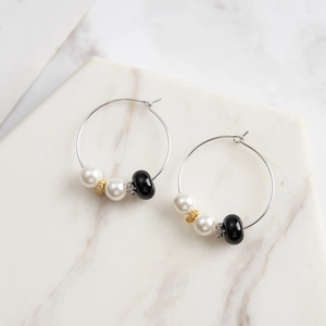 Macro shot of silver earrings with white pearls and black obsidian on marble background