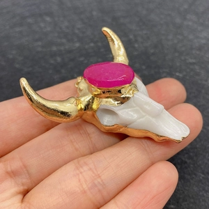 Dettaglio del ciondolo a teschio di toro con corna dorate e gemma ovale rosa