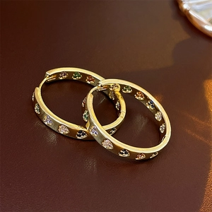 Macro shot of gold hoop earrings with colorful zircon hearts on brown leather