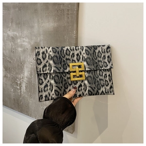 Detail view of leopard print clutch featuring a gold H-shaped metal buckle on grey texture
