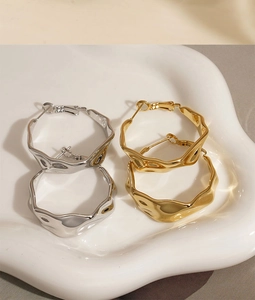 Detailed view of gold and silver irregular C-shape wrinkled earrings on a ceramic tray