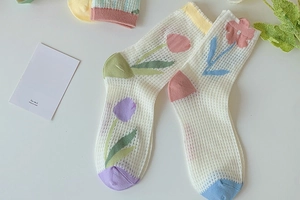 Macro detail of white breathable mesh socks featuring pastel tulip and flower embroidery