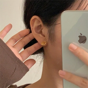 Minimalist gold knot stud earrings shown in a realistic mirror selfie style on ears