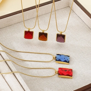 Macro shot of colorful square crystal pendants on gold snake chains in a jewelry tray
