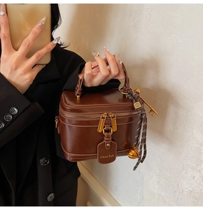 Detail of dark brown leather vanity bag with gold zippers and decorative tassel charm