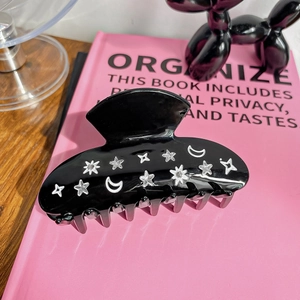 Detail of black acetate hair claw clip featuring sparkling rhinestone star and moon motifs