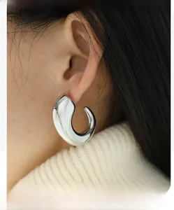 Close-up of chunky silver C-shape earrings on a model with a knit sweater backdrop
